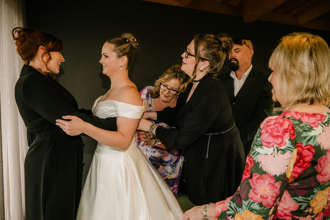Jessica in her gown surrounded by women helping with the final touches