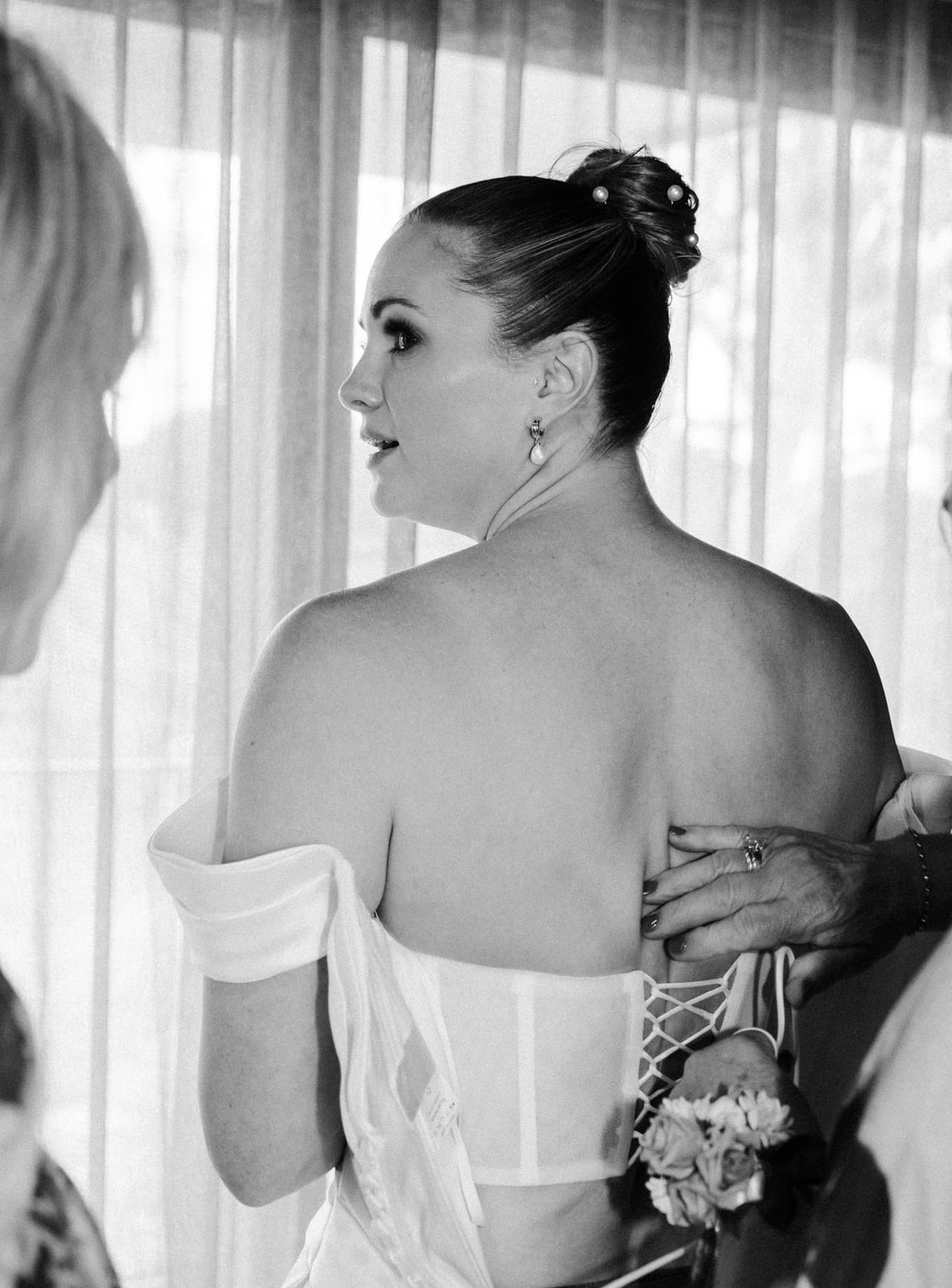 Black and white photo of Jessica looking out of the window while her dress is laced up