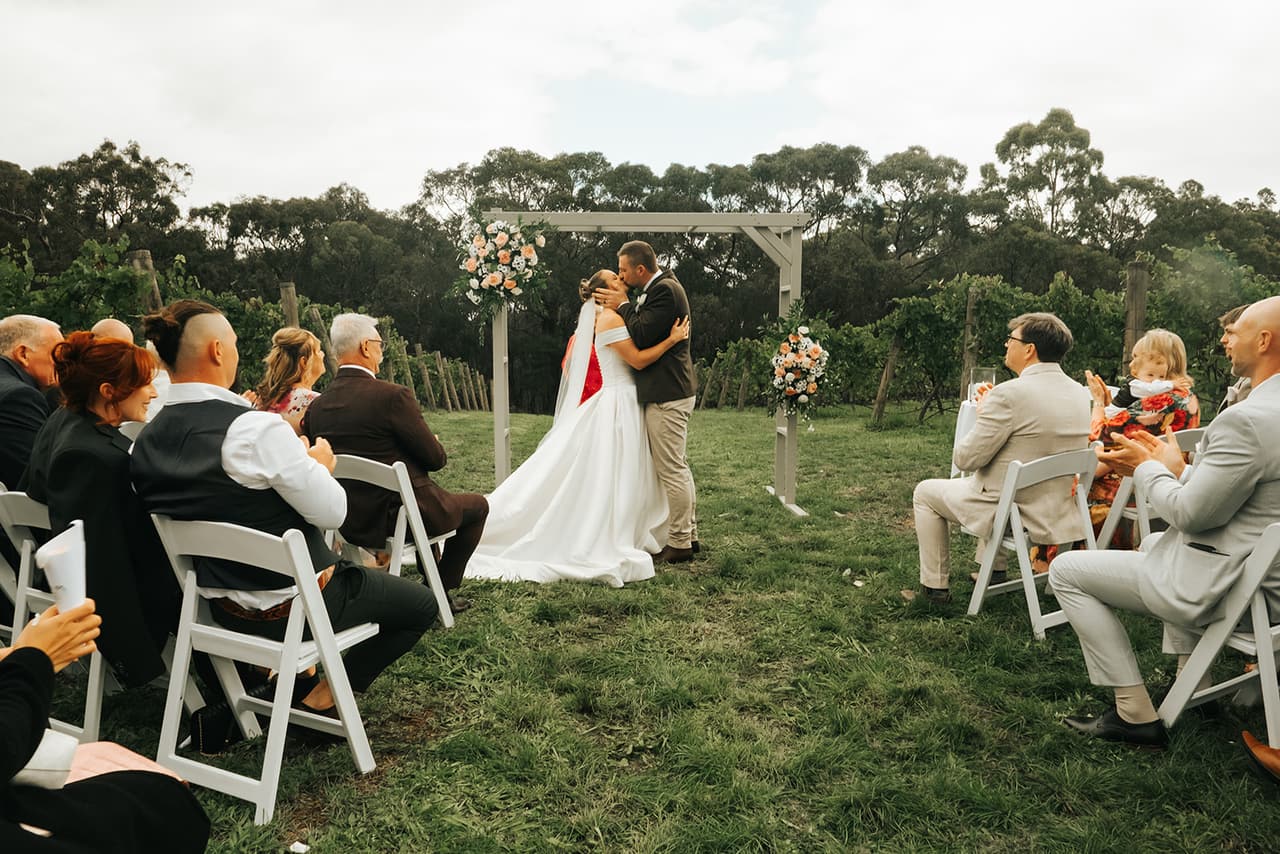 Jessica and Max’s first kiss under the arbour, seen from behind the seated guests