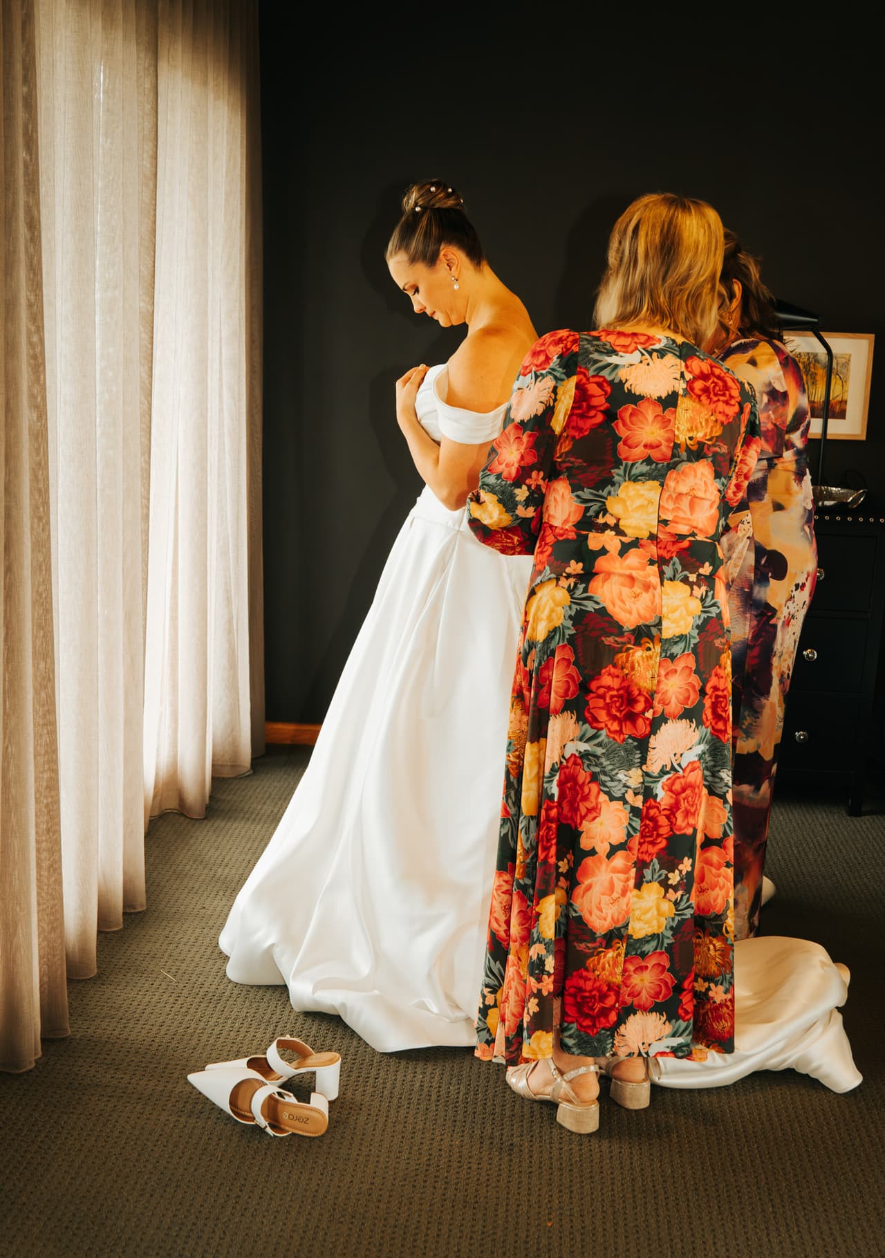 Jessica getting ready while a woman in a floral dress adjusts her gown