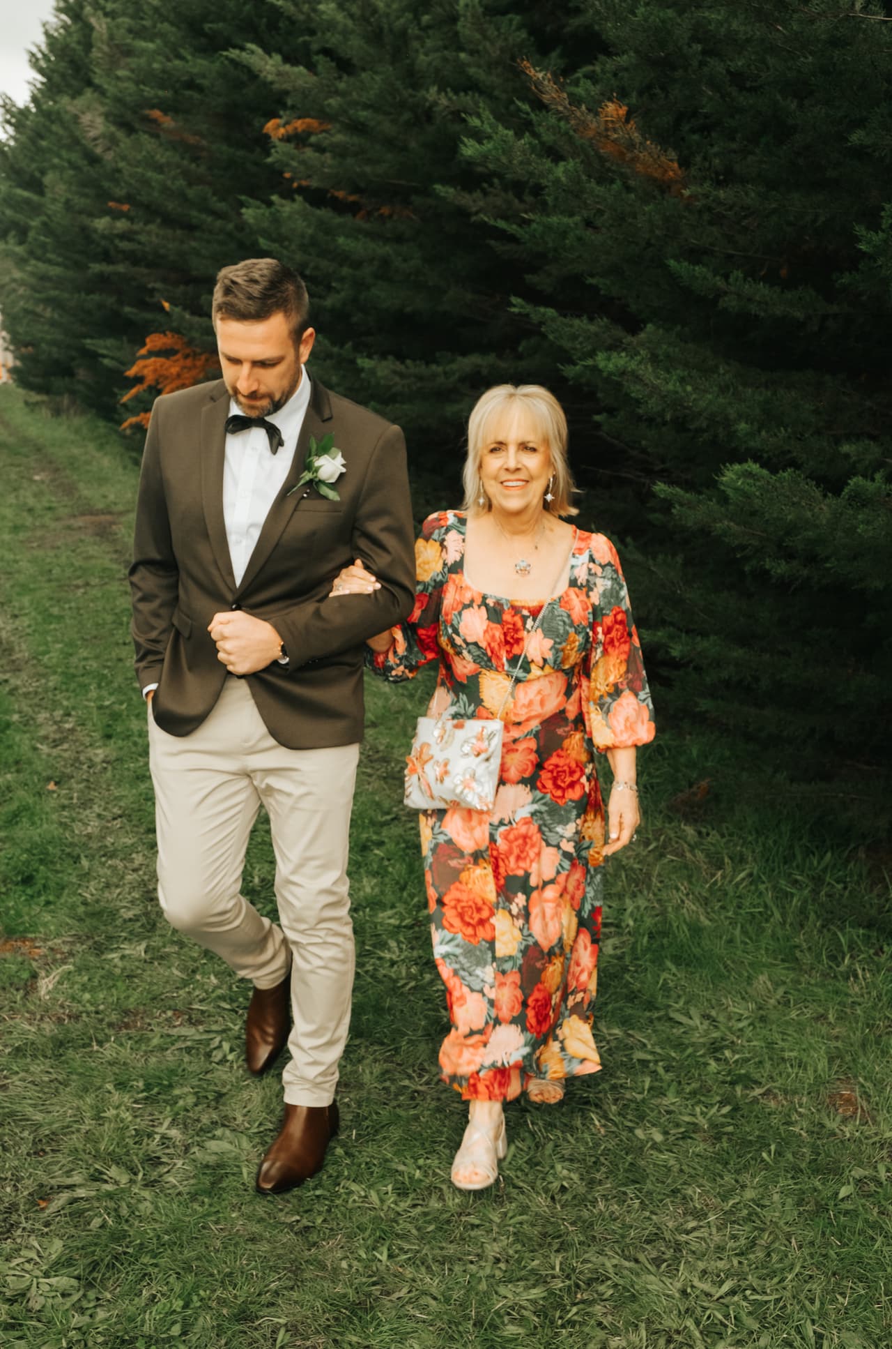 Max walking down the grassy aisle between the vines with a woman in a bright floral dress