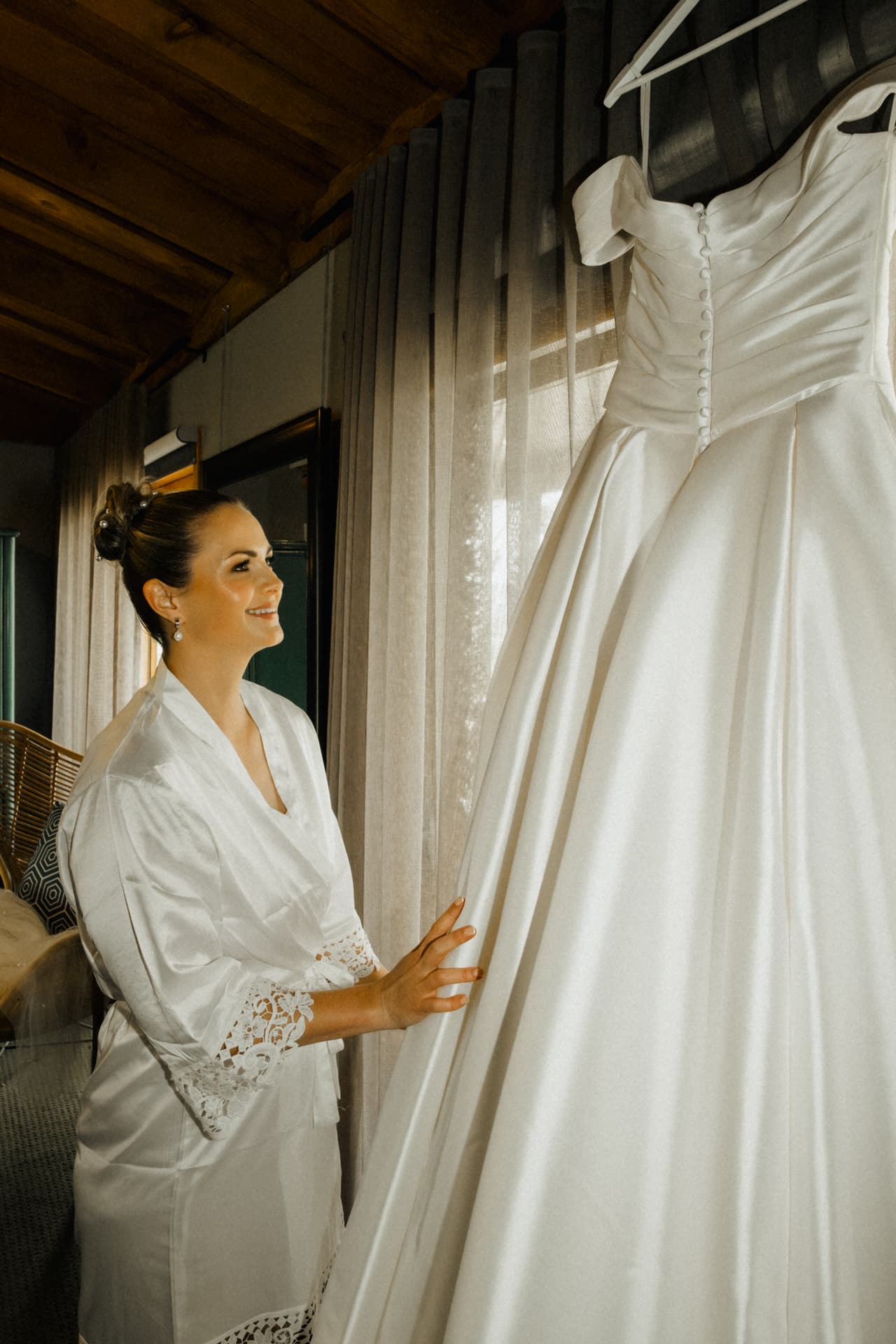 Jessica in a white robe smiling at her gown hanging in the window
