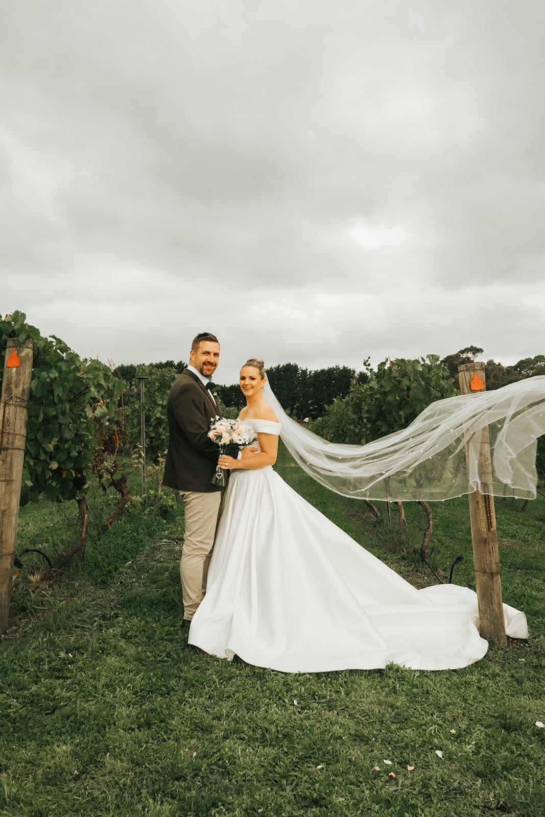 Jessica’s long veil lifting in the wind as she and Max stand between the vines