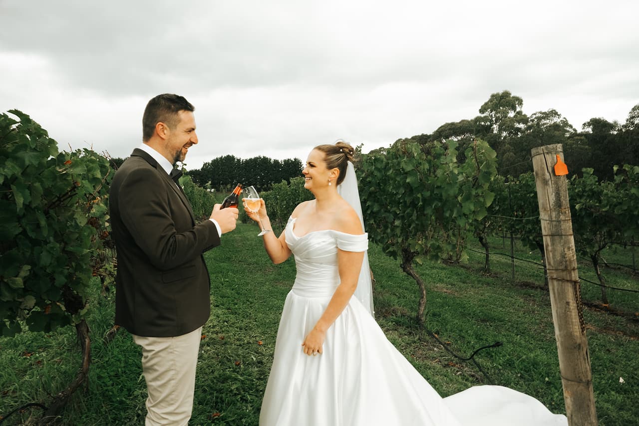 Jessica and Max clinking glasses between the rows of vines