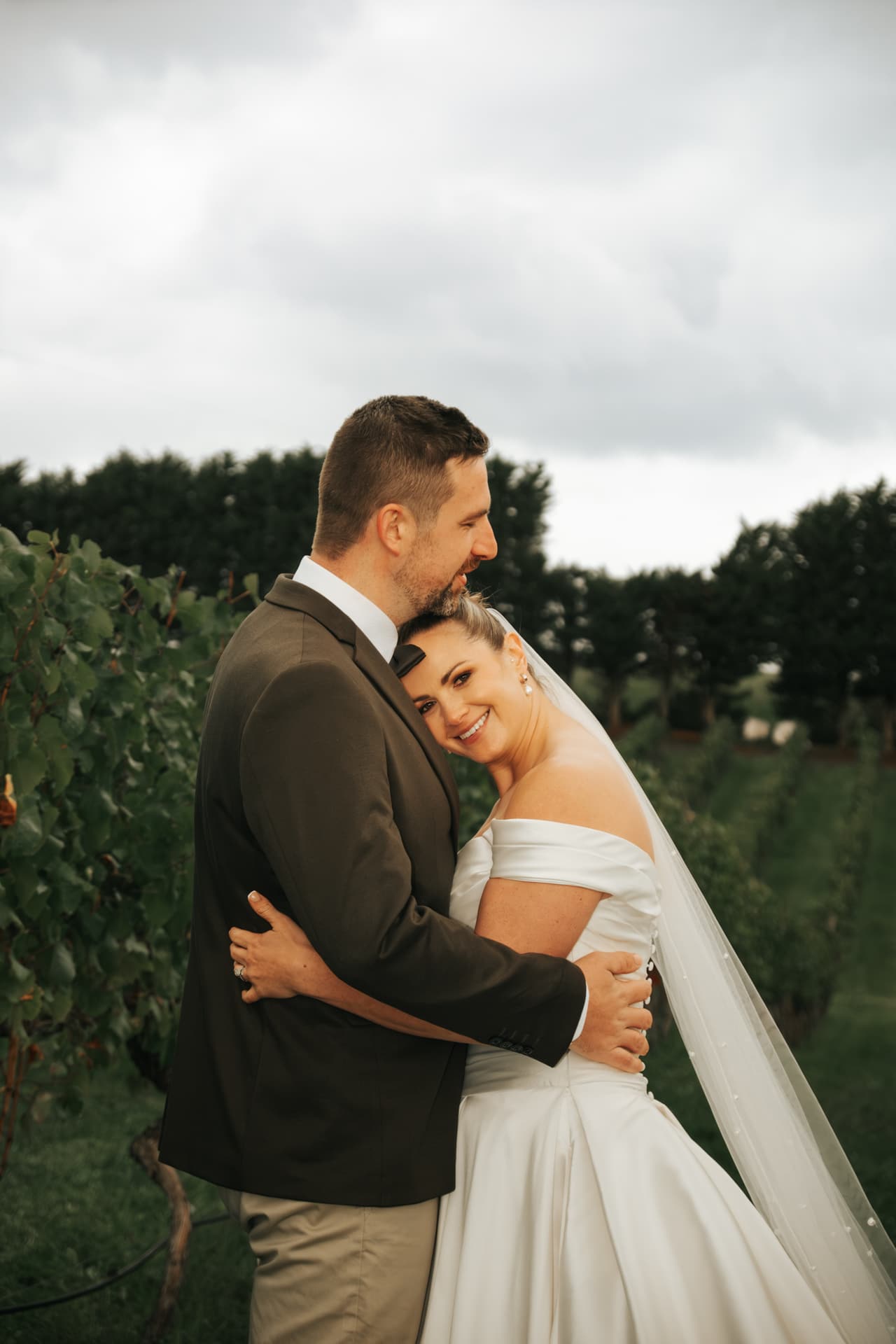 Max holding Jessica close among the vines on a cloudy afternoon, her head resting on his chest