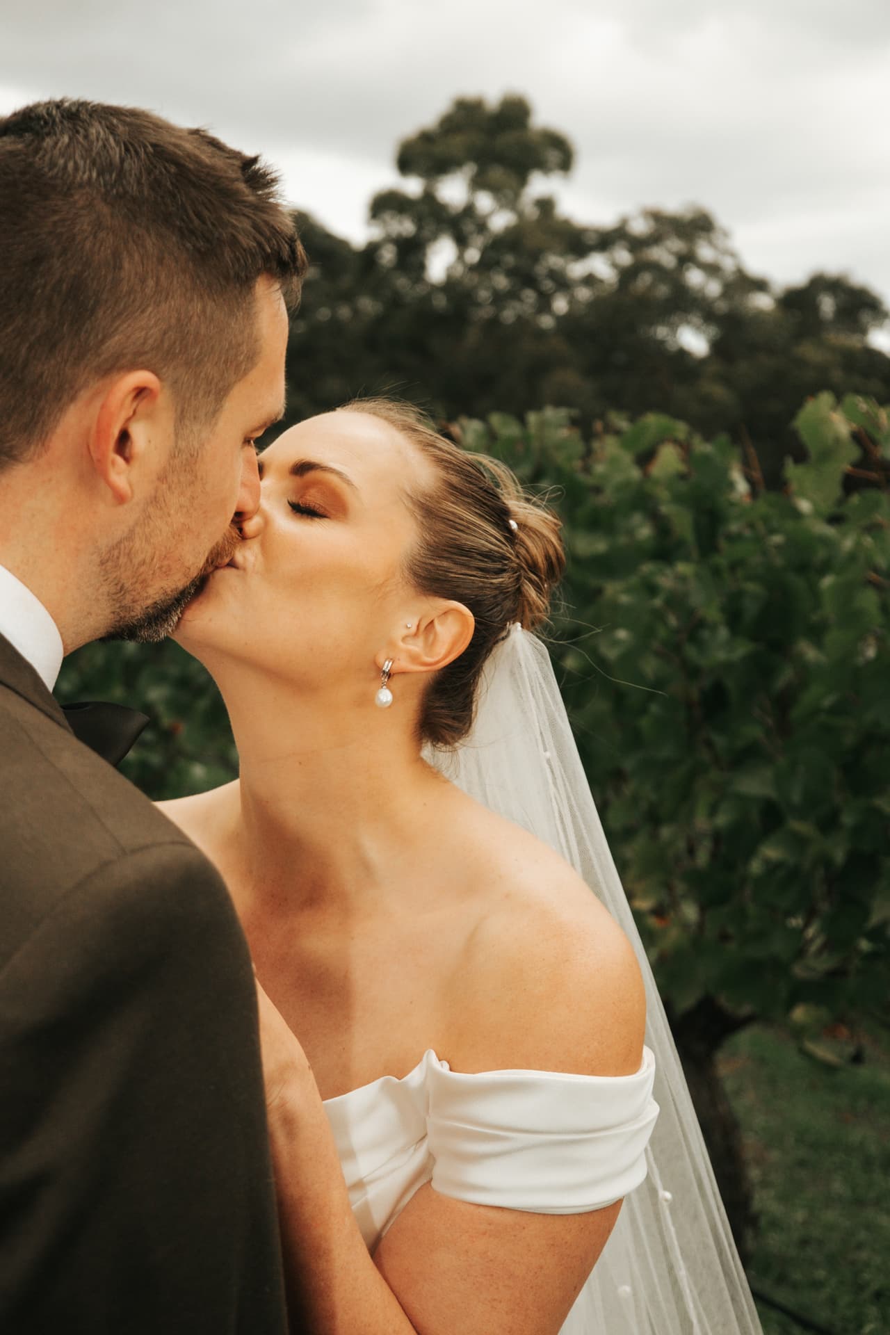 Jessica and Max kissing among the vines, her veil trailing behind her