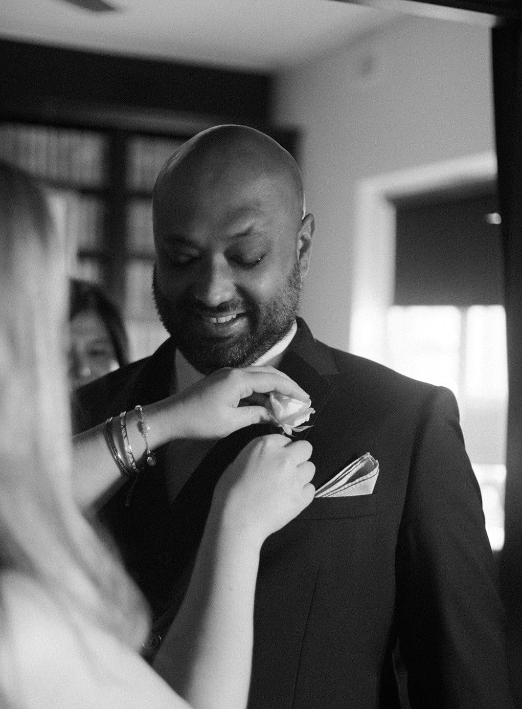 Black and white photo of a white rose buttonhole being pinned to Krish’s jacket