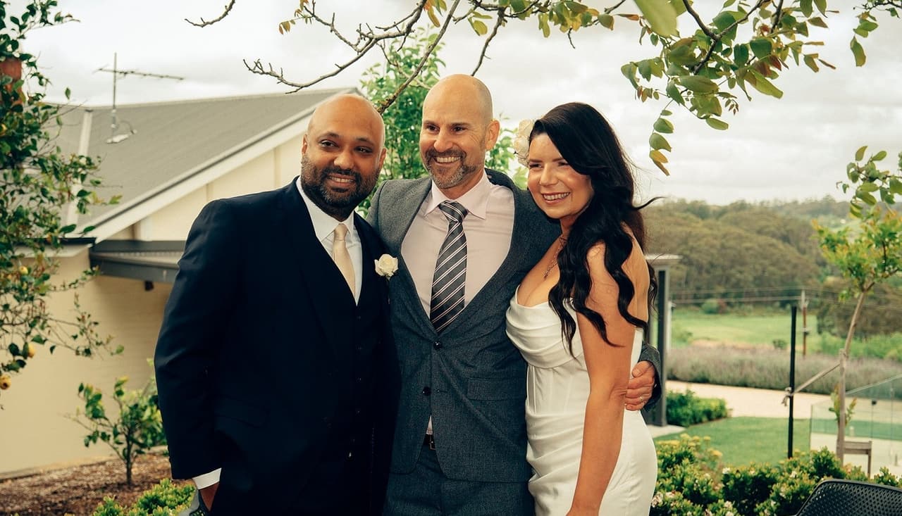 Krish and Joanna with the celebrant on the lawn, the hills behind them