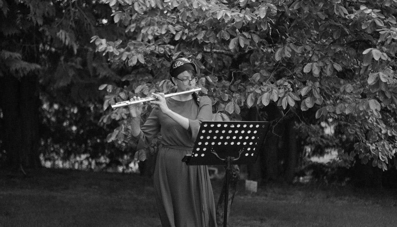 Black and white photo of a flute player at a music stand under the trees in the garden
