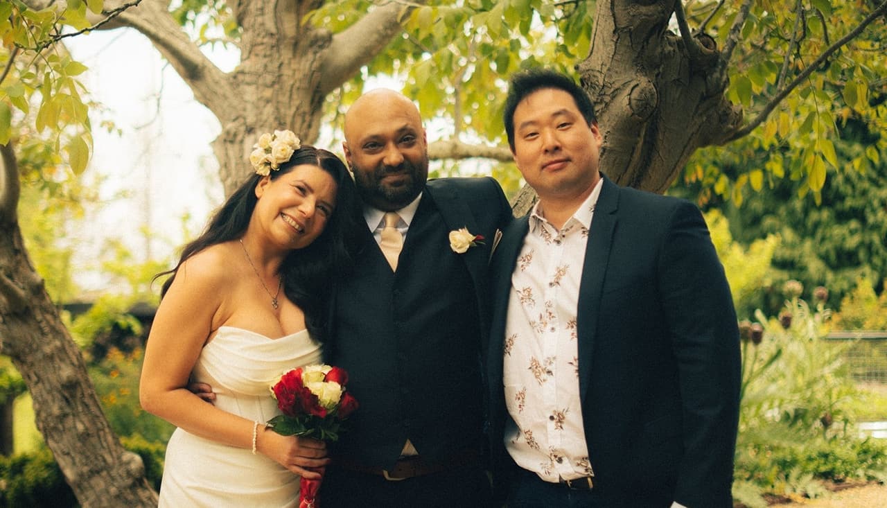 Joanna and Krish under the tree with a guest in a dark jacket