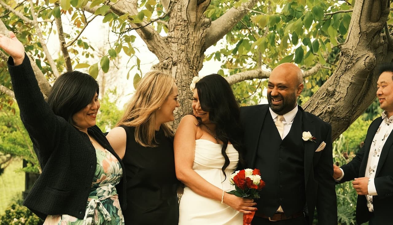 A guest cheering beside Joanna and Krish under the tree