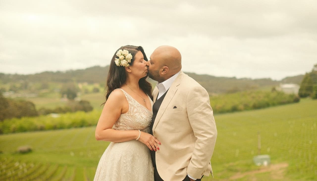 Joanna kissing Krish on the cheek with the rolling green hills behind them