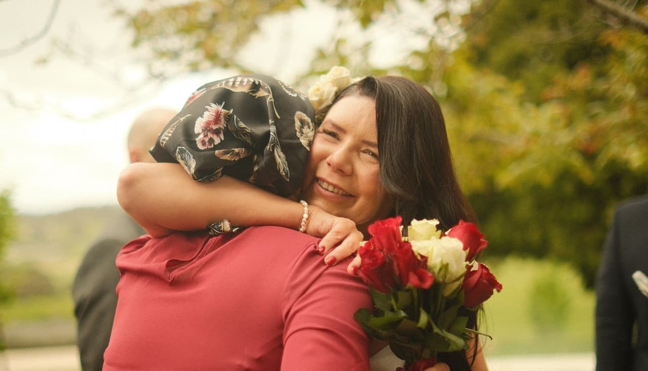 A guest in a red dress hugging Joanna, who holds her roses