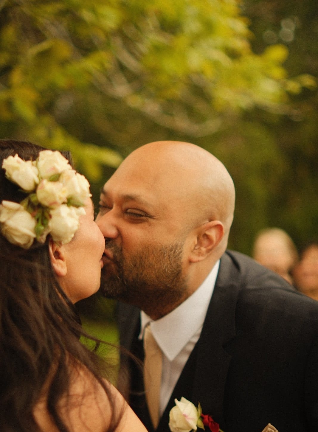 Krish kissing Joanna, who has white roses in her hair, as guests look on