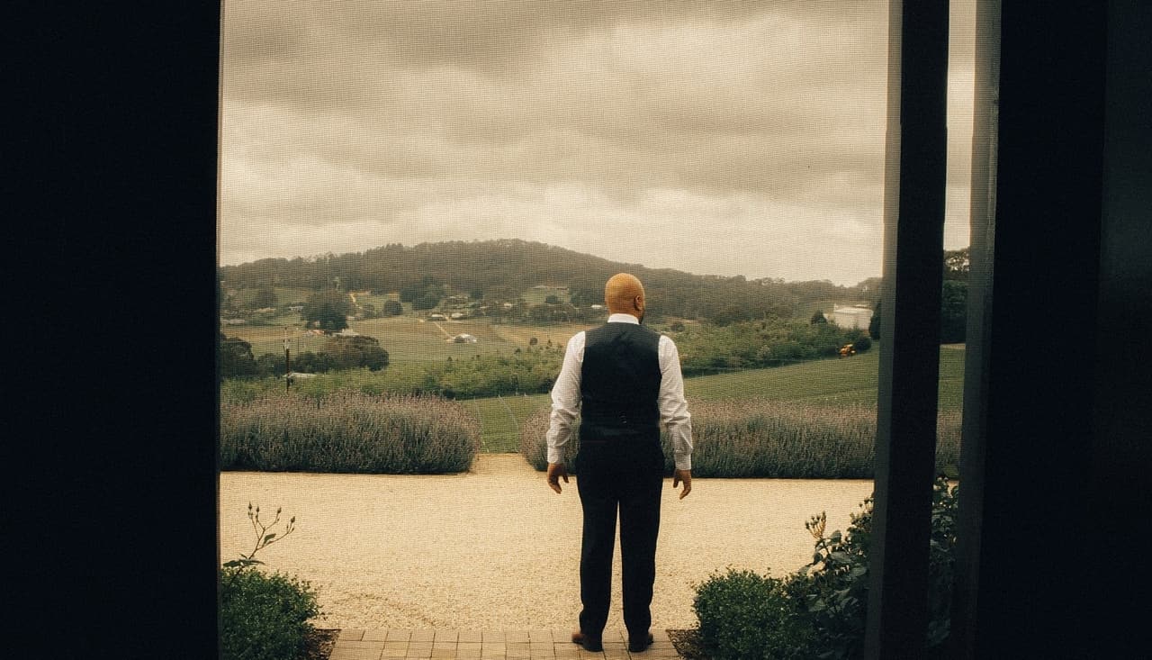 Krish standing in an open doorway, looking out over the lavender to the green hills