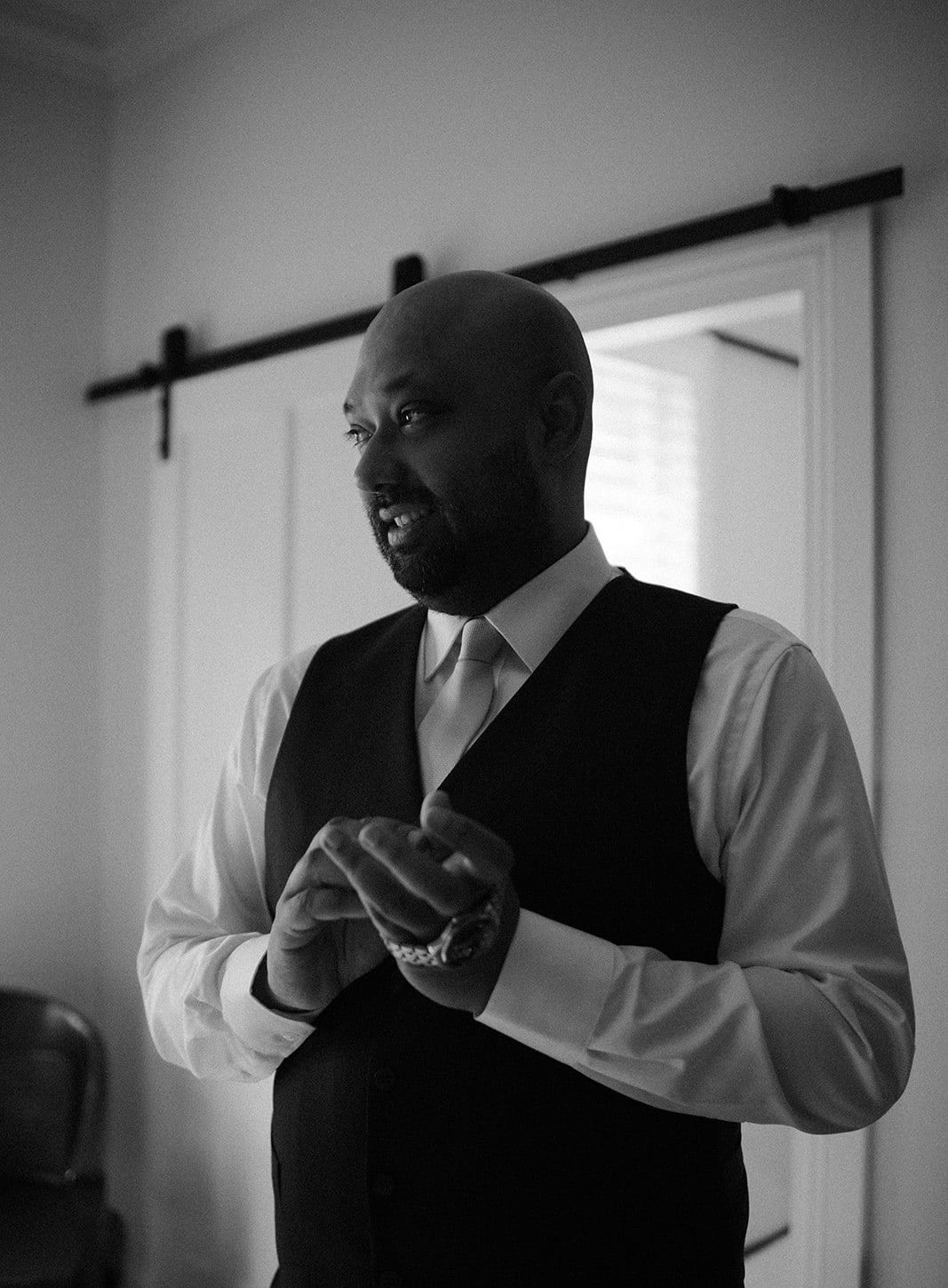 Black and white photo of Krish in his waistcoat by a window, doing up his cuffs