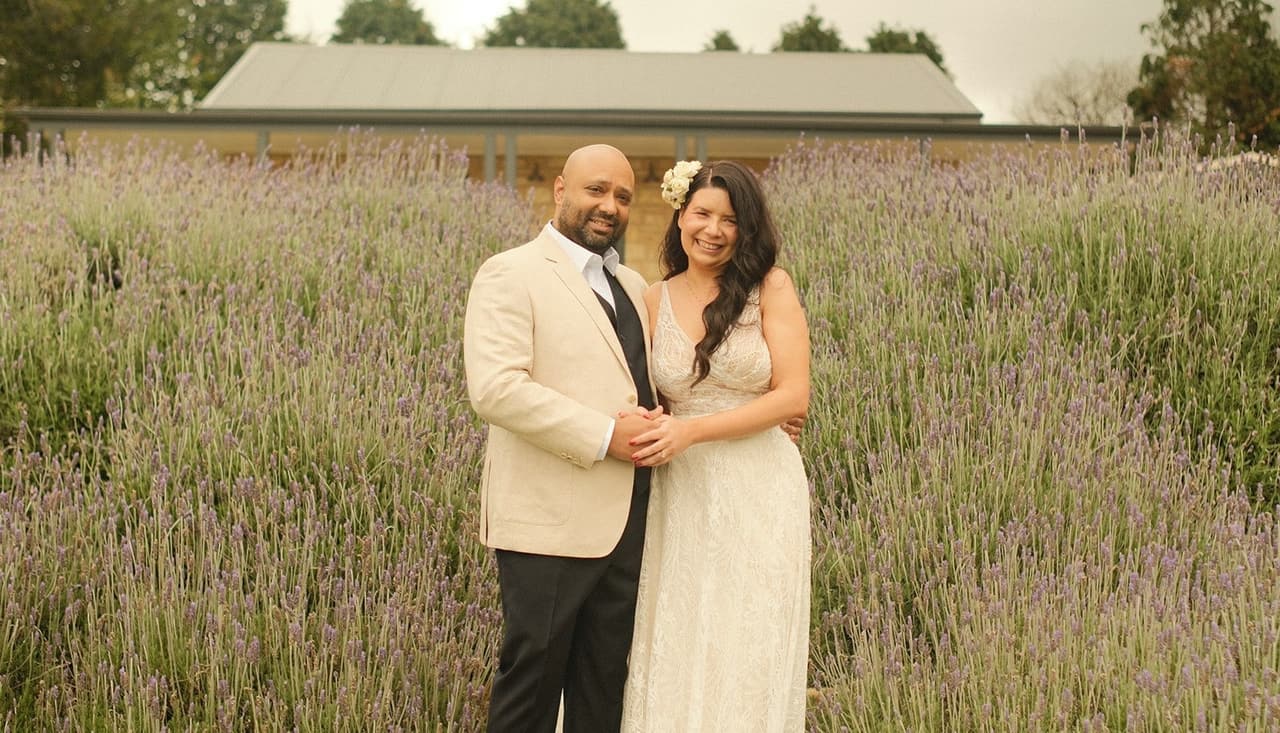 Krish in a cream jacket and Joanna in a lace gown standing in the lavender