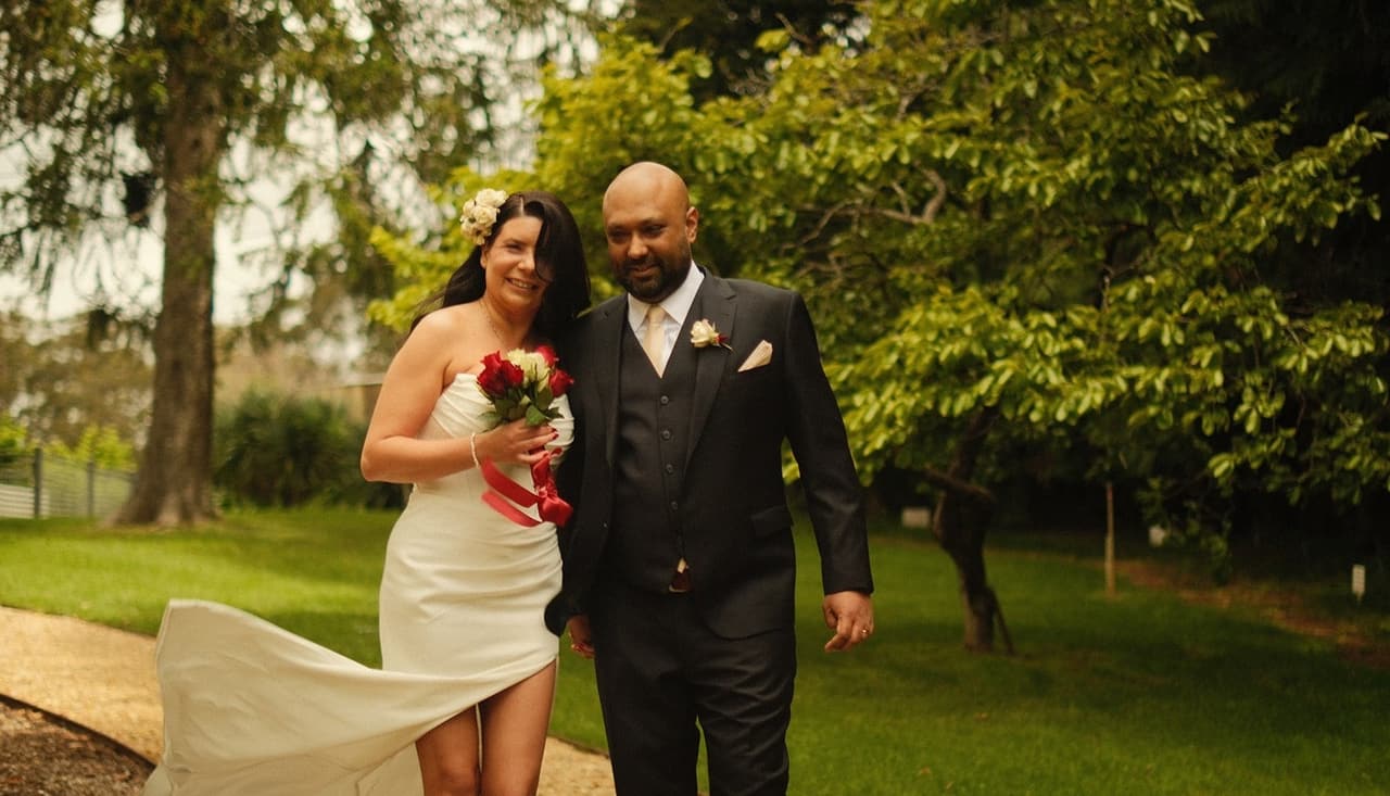 Joanna and Krish walking across the lawn, her gown catching the breeze