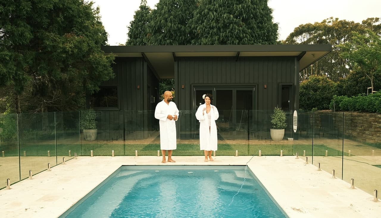Joanna and Krish in white robes at the end of the pool