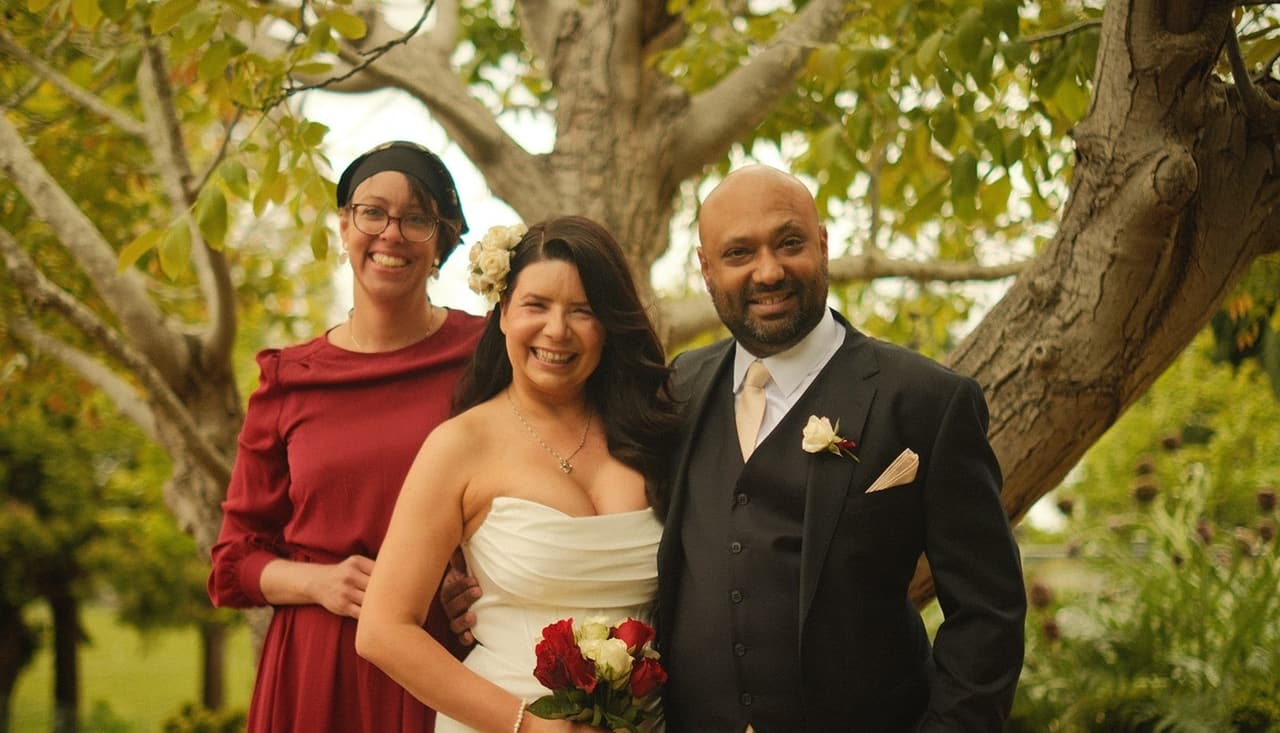 Joanna and Krish under the tree with a guest in a red dress