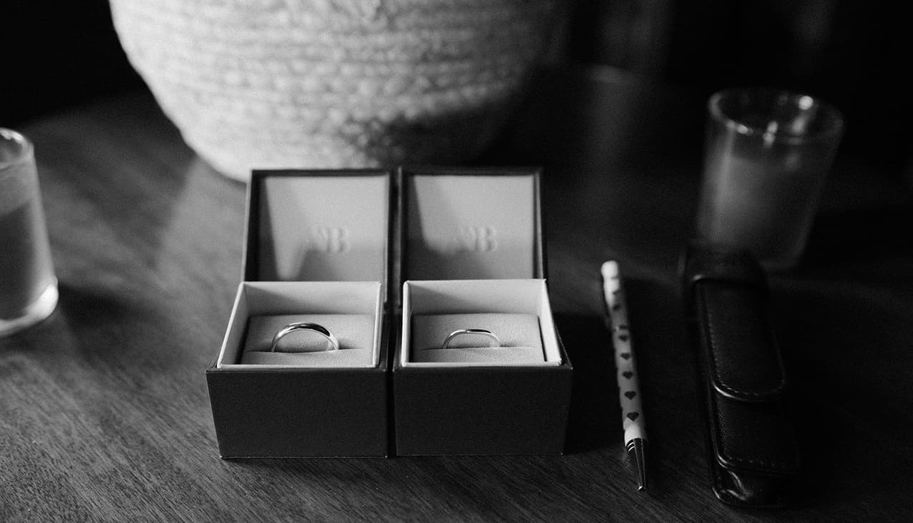 Black and white photo of two wedding rings in their boxes beside a pen with little hearts