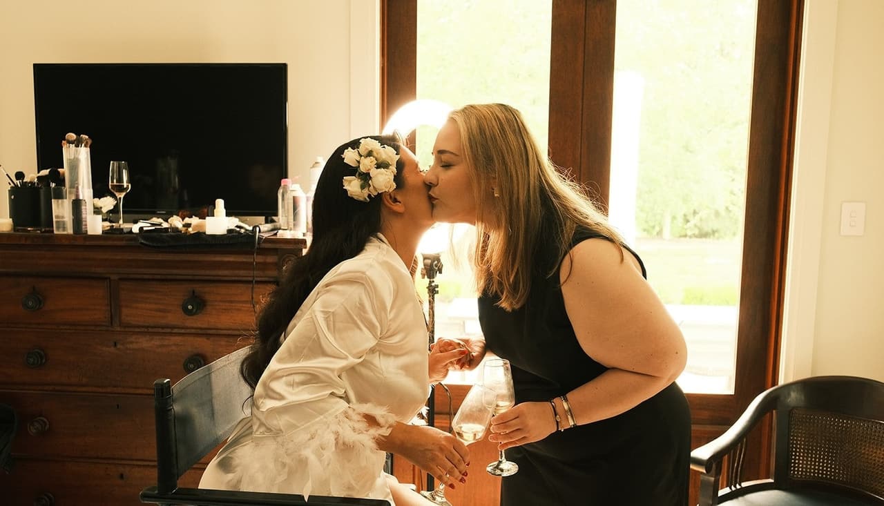 A woman in a black dress kissing Joanna on the cheek as she sits in her robe