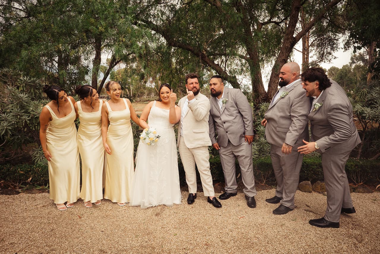 The bridal party laughing together on the gravel in front of the old trees