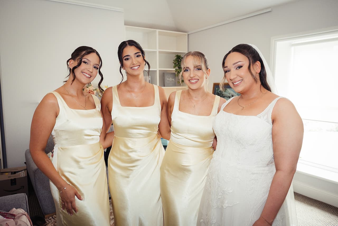 Karina in her gown with her three bridesmaids in champagne satin, arm in arm in the bridal room