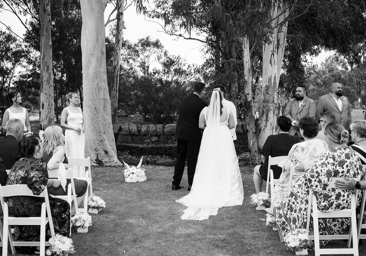 Black and white photo of Karina and her dad reaching the front of the aisle, seen from behind the guests