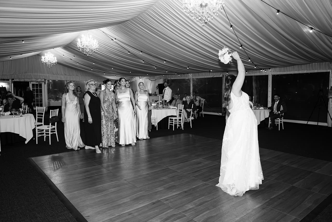 Black and white photo of Karina tossing her bouquet over her shoulder on the dance floor