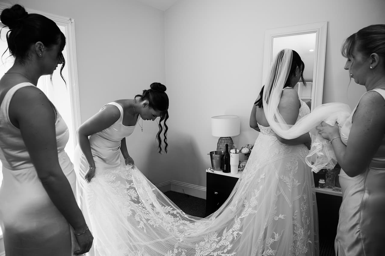 Black and white photo of the bridesmaids bustling Karina’s train after the ceremony