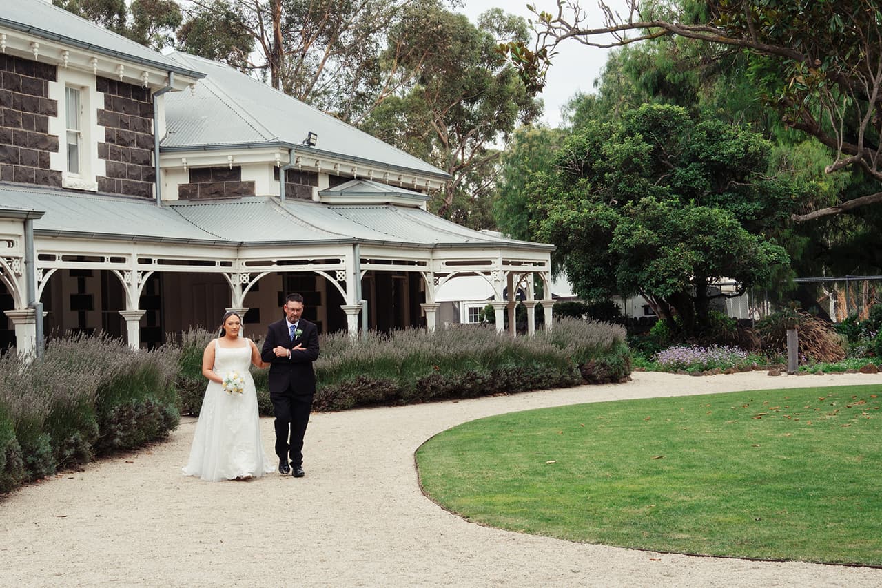 Karina on her dad’s arm, walking the curved gravel path from the homestead to the ceremony
