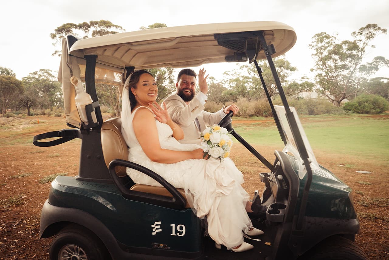 Karina and Bronson laughing in a golf cart on the grounds, Bronson waving