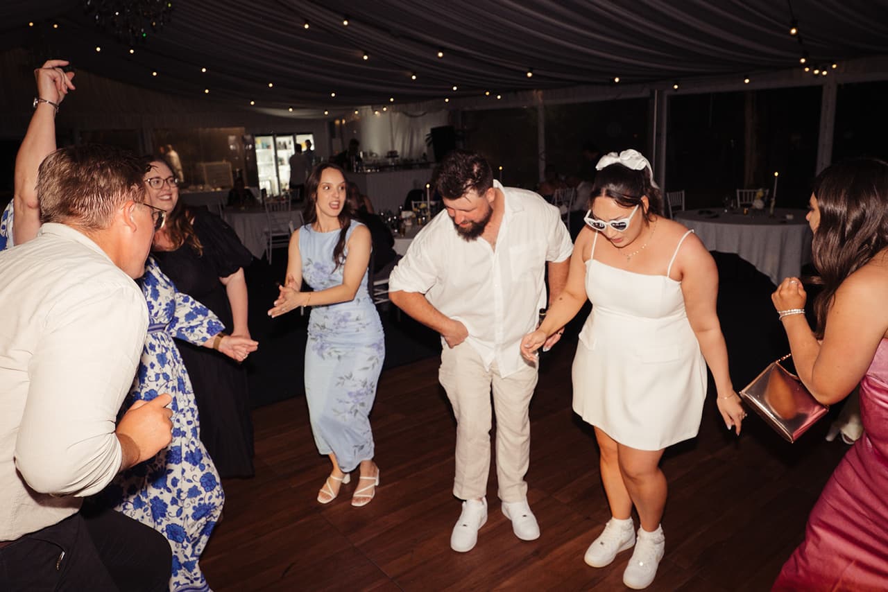 Karina in a short white party dress dancing with Bronson and their friends