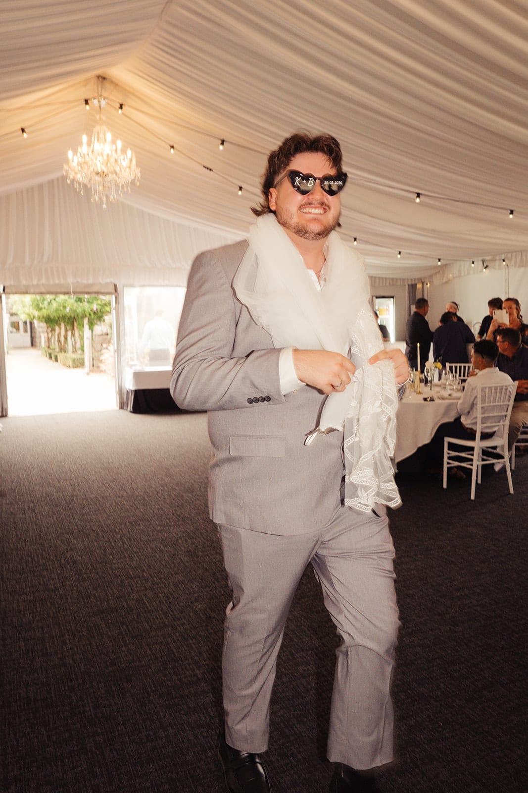 A groomsman in sunglasses swinging a white napkin as he dances into the marquee