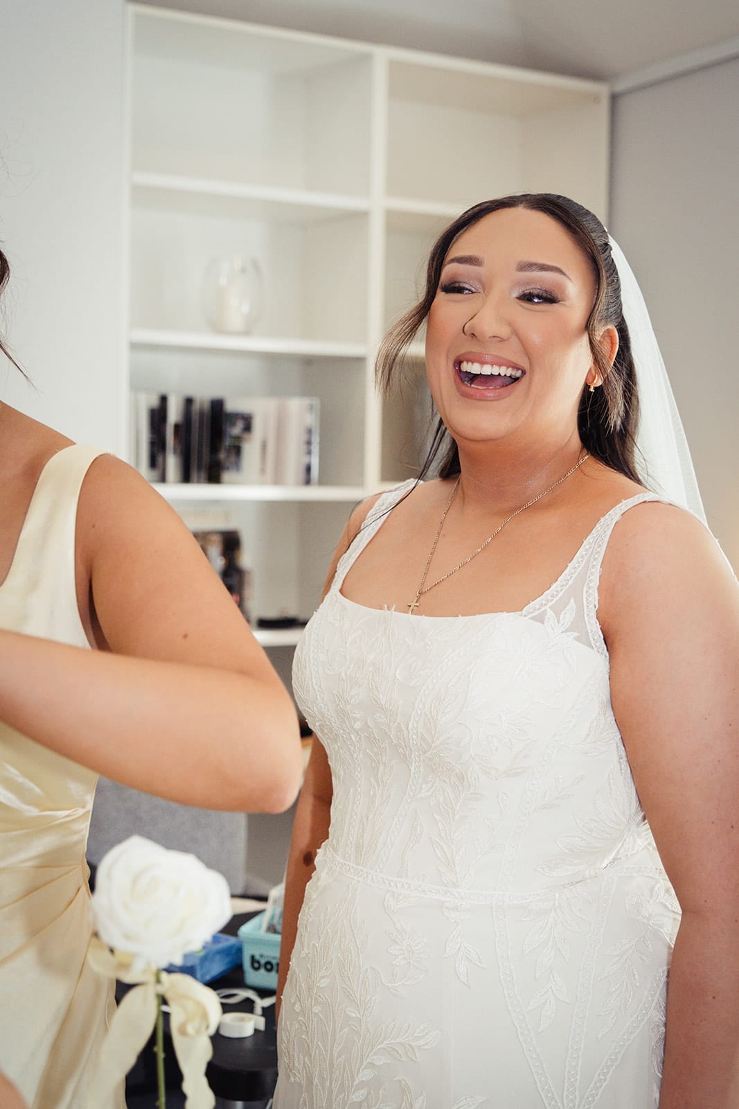 Karina laughing in her gown and veil beside the white bookshelves