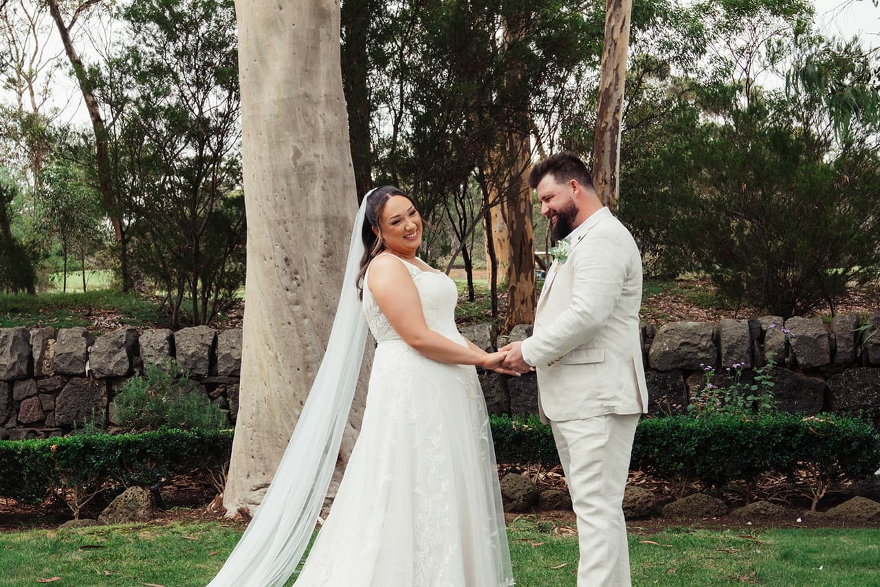Karina and Bronson holding hands under the tall gums, the old stone wall behind them