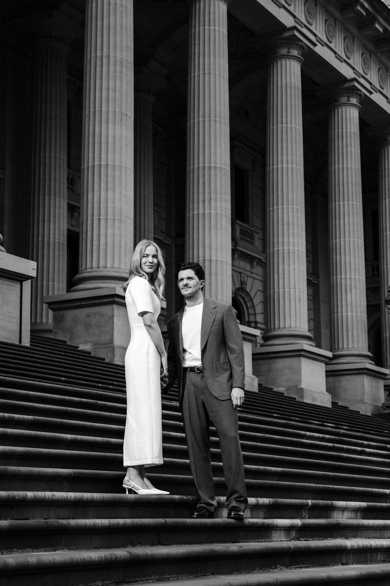 Black and white photo of Karina and Chris on the wide steps beneath the columns of Parliament House