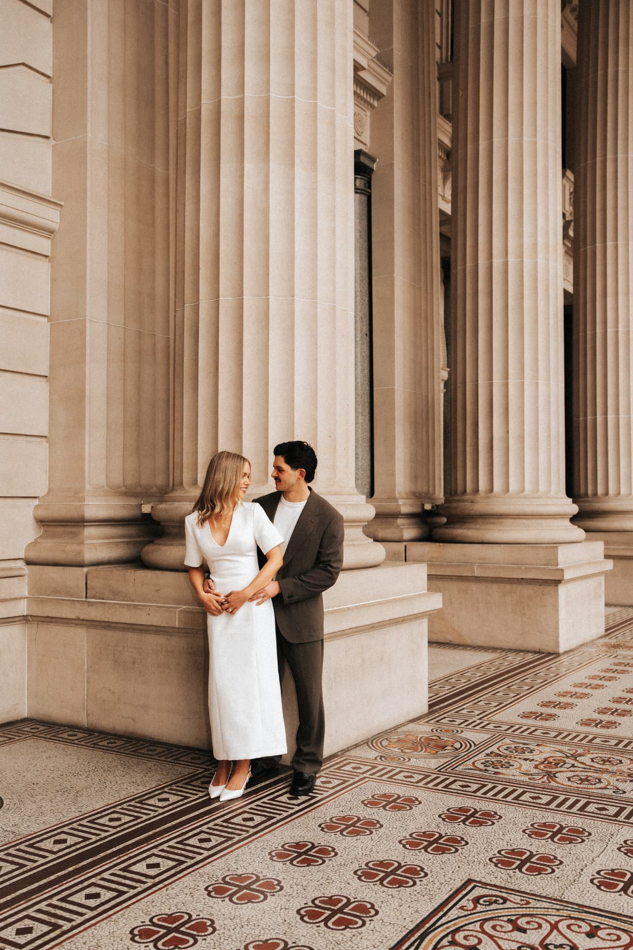 Karina and Chris in the long colonnade of Parliament House, patterned tiles at their feet