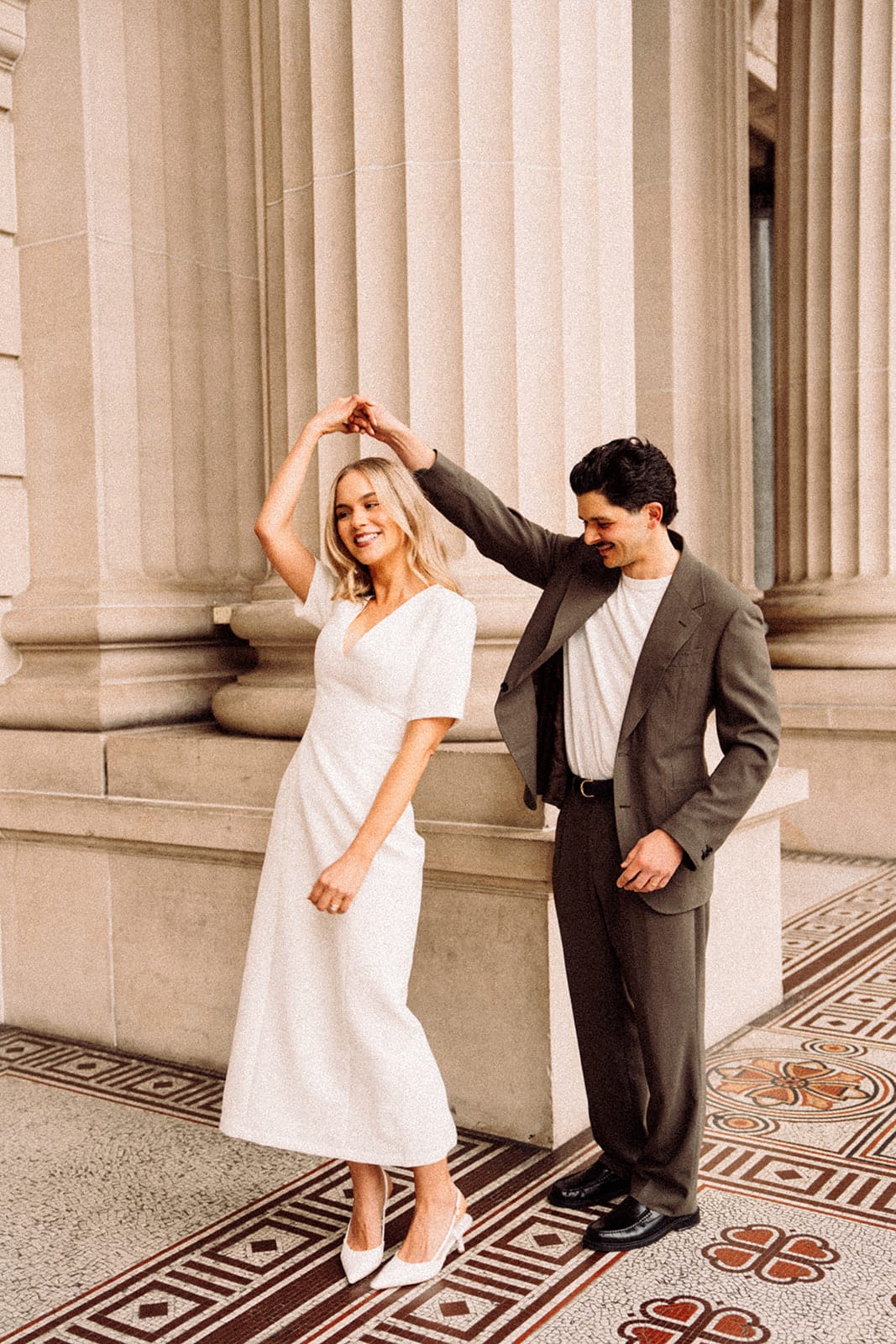 Chris twirling Karina under the colonnade of Parliament House, patterned tiles at their feet