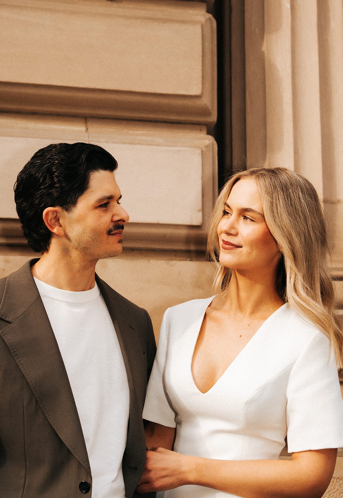 Karina and Chris smiling at each other against the sandstone columns of the Old Treasury Building