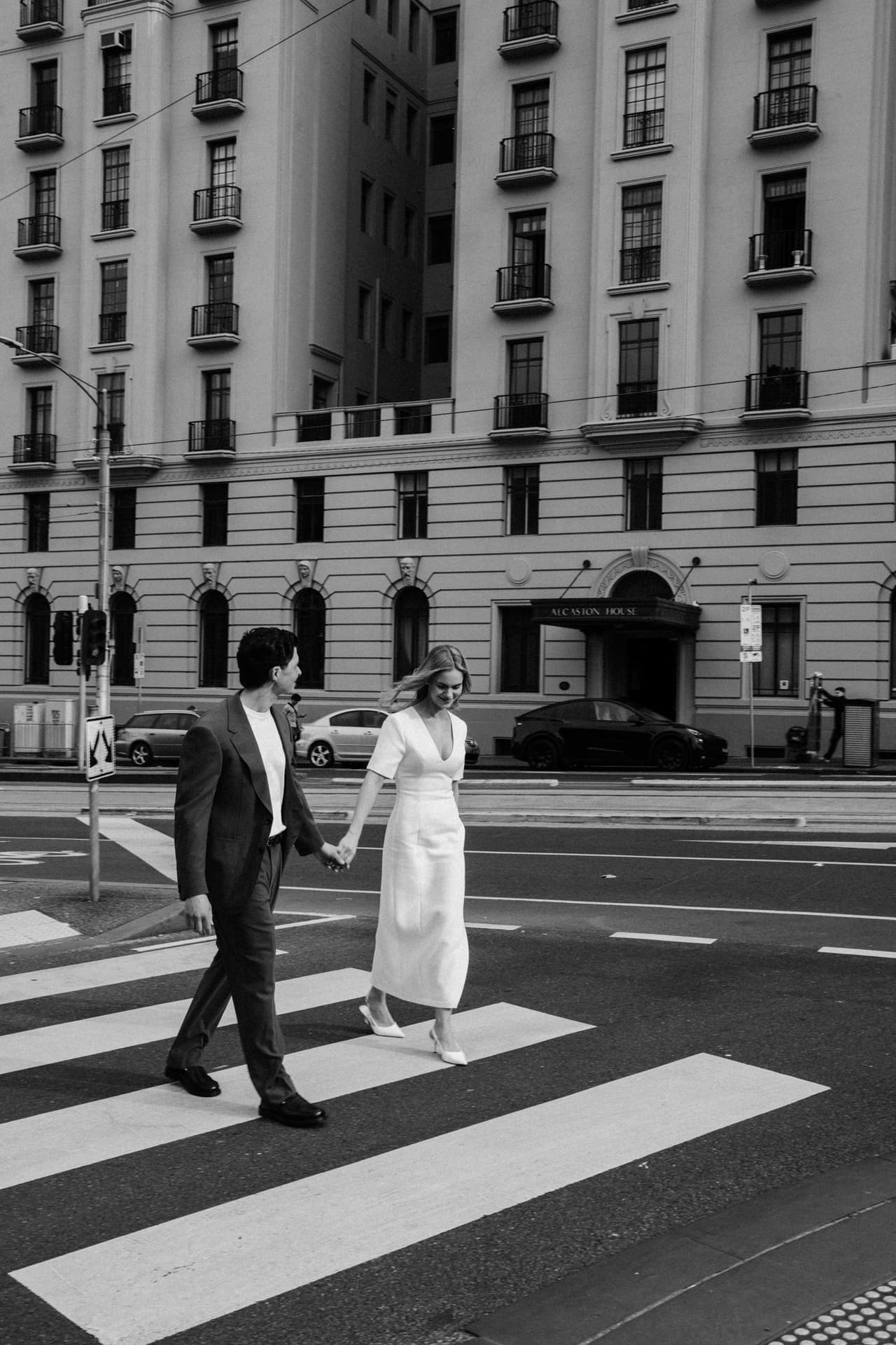 Black and white photo of Karina and Chris crossing a city street hand in hand at a zebra crossing
