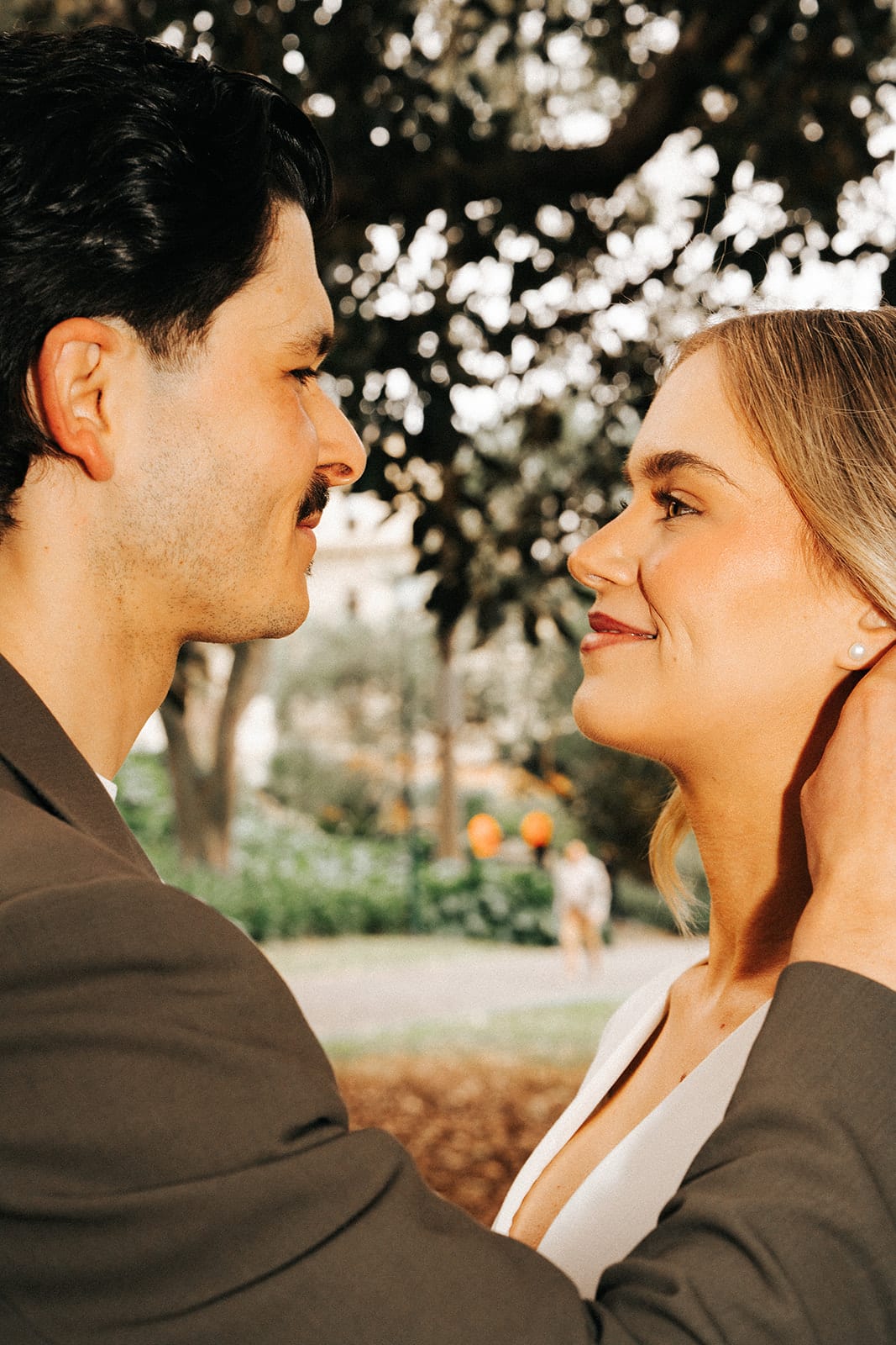 Karina and Chris smiling at each other under the trees of Treasury Gardens