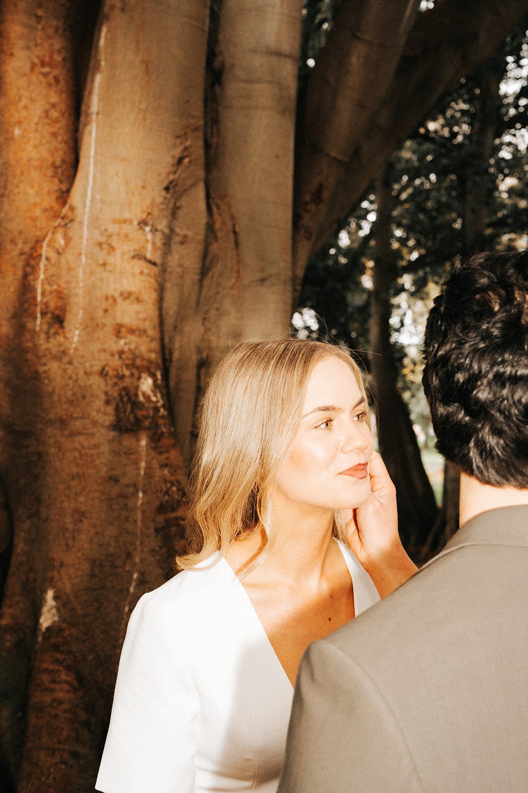 Karina with her hand to her face beside the trunk of a huge fig tree, Chris close beside her