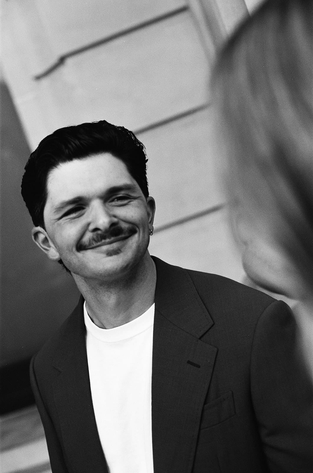 Black and white portrait of Chris smiling beside a column, on 35mm film
