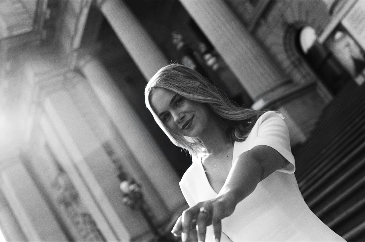 Black and white photo of Karina reaching a hand back to the camera on the steps of Parliament House, on 35mm film