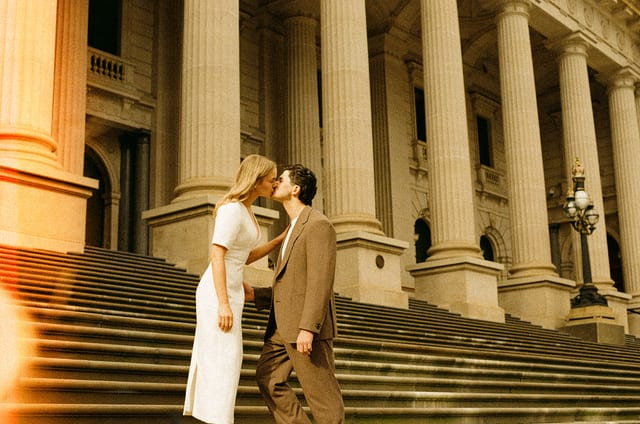 Karina and Chris kissing on the sandstone steps of Parliament House in golden light, on 35mm film