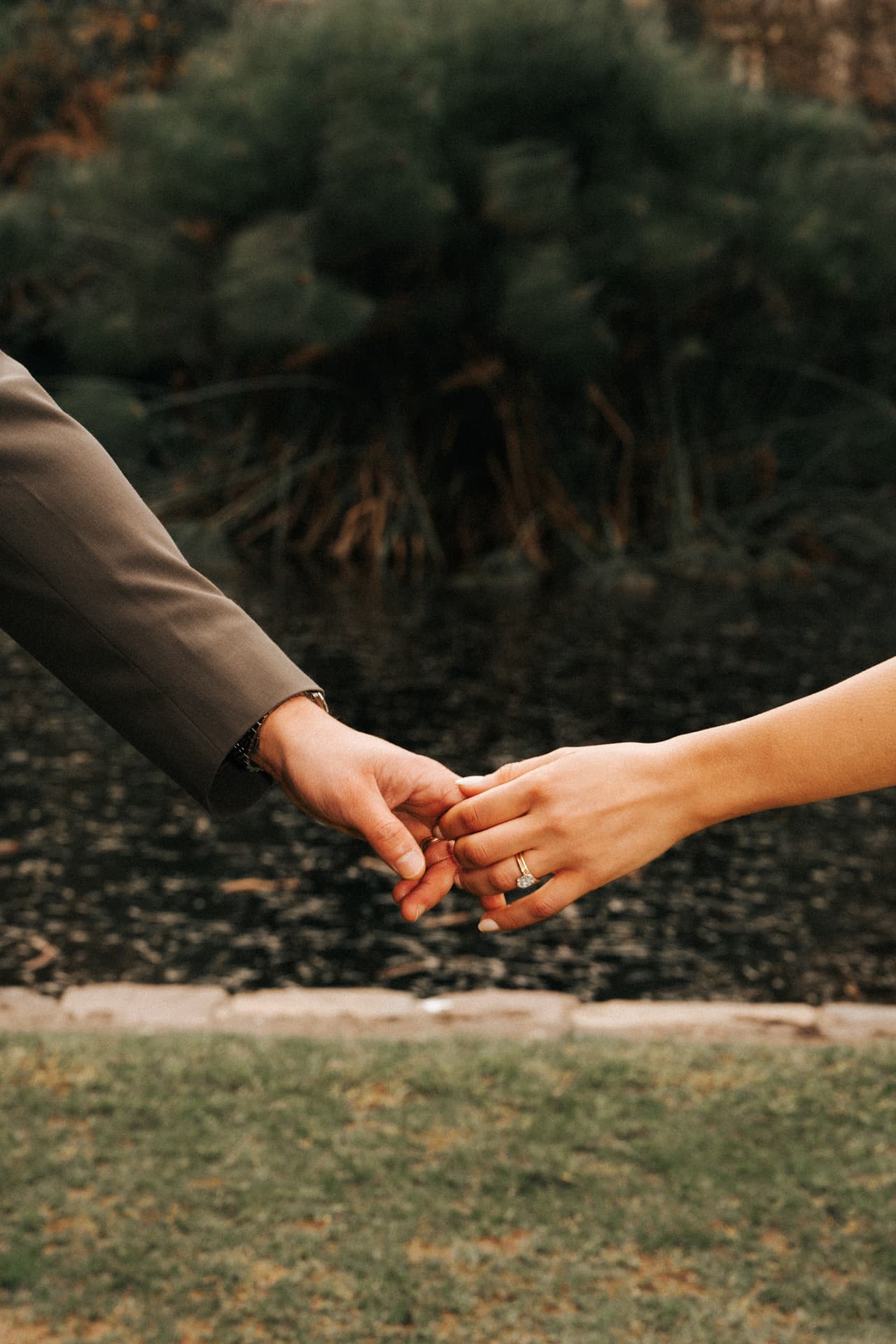 Close up of Karina and Chris reaching for each other’s hands above the lawn, her ring catching the light