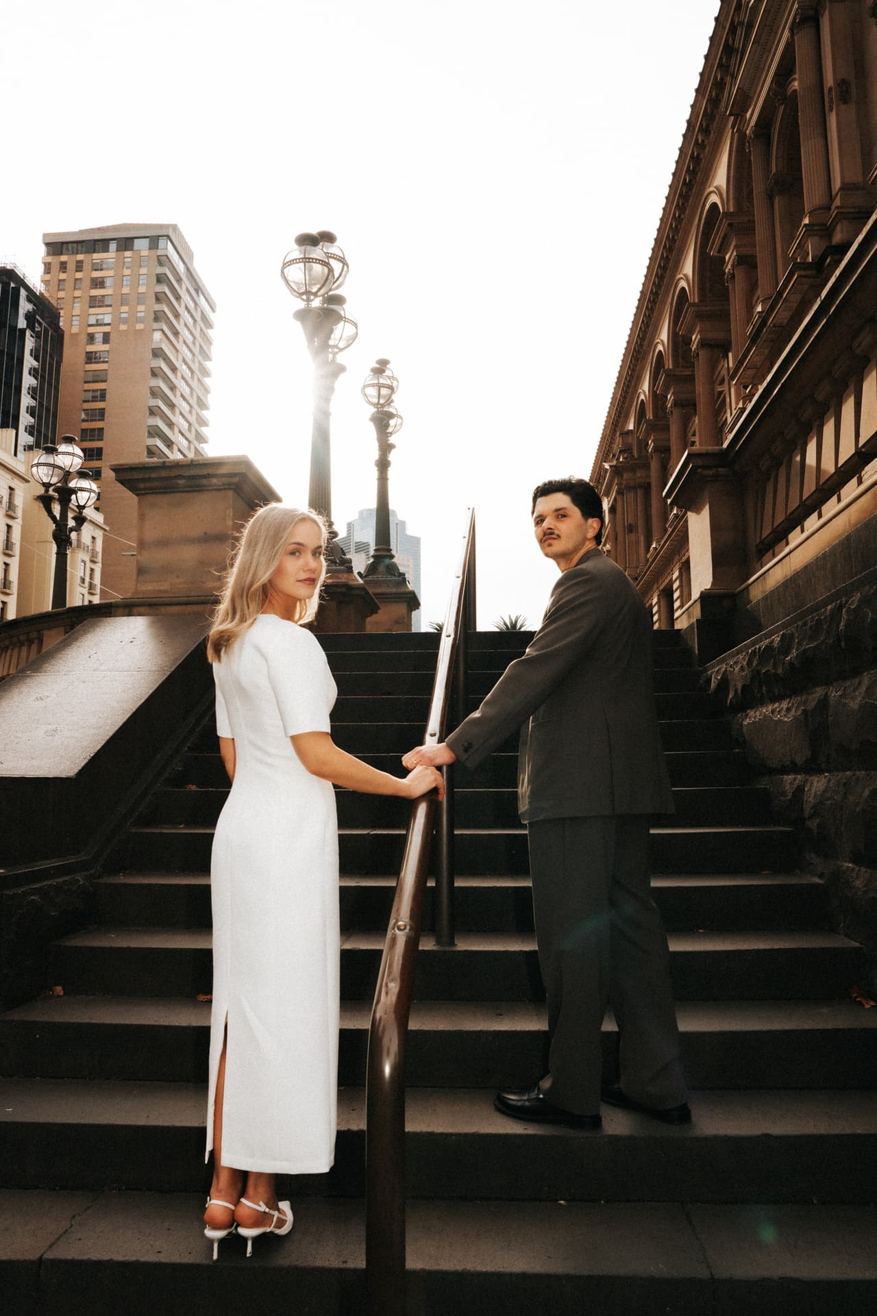 Karina and Chris holding hands on the stone steps beside the Old Treasury Building, Karina looking back at the camera