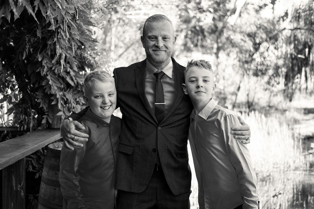 Black and white photo of Ben with an arm around each of two boys on the deck